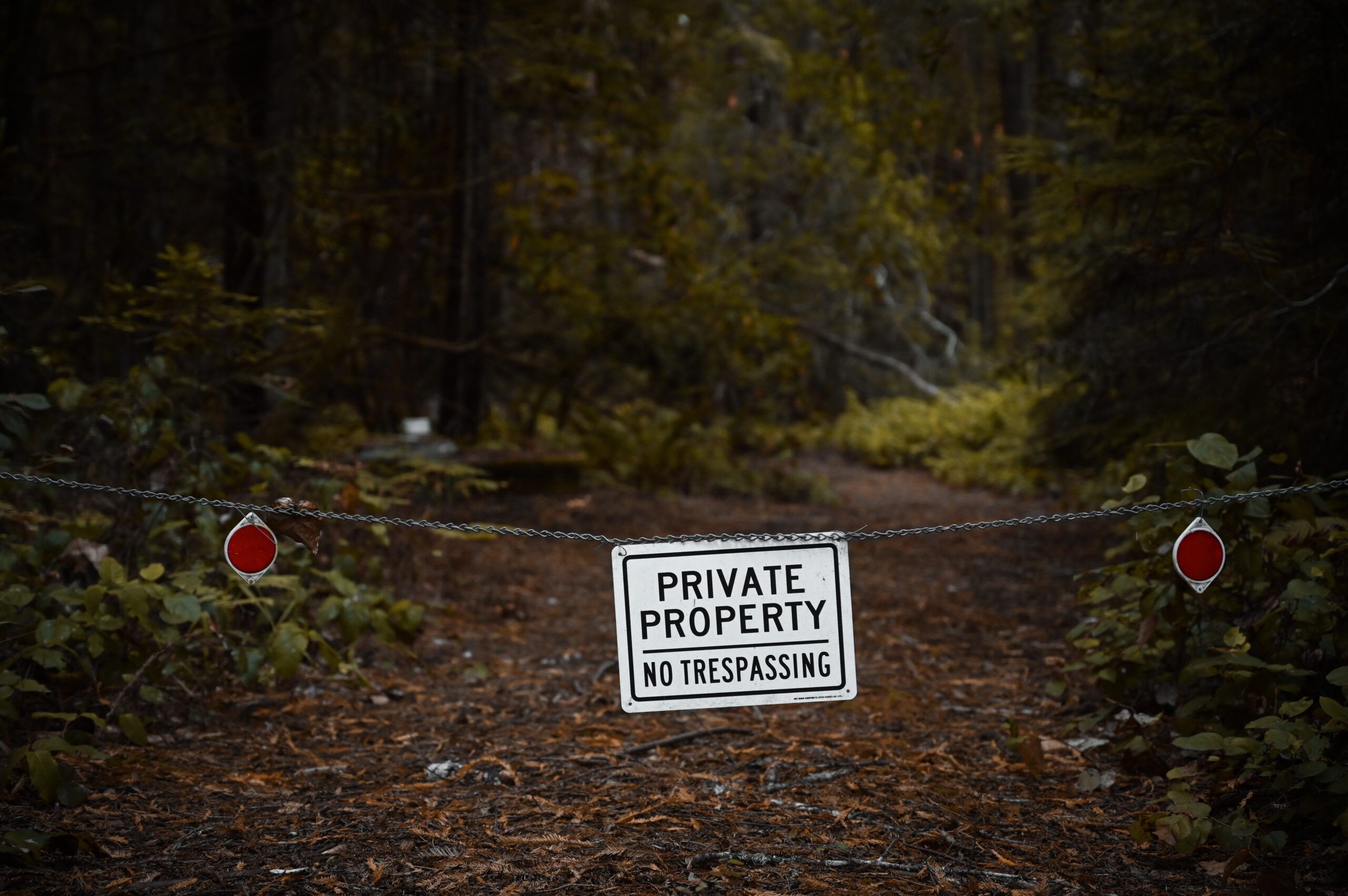 A stock photo of a chain fence stretched across a path, with a sign reading "private property no trespassing" stretched across it.